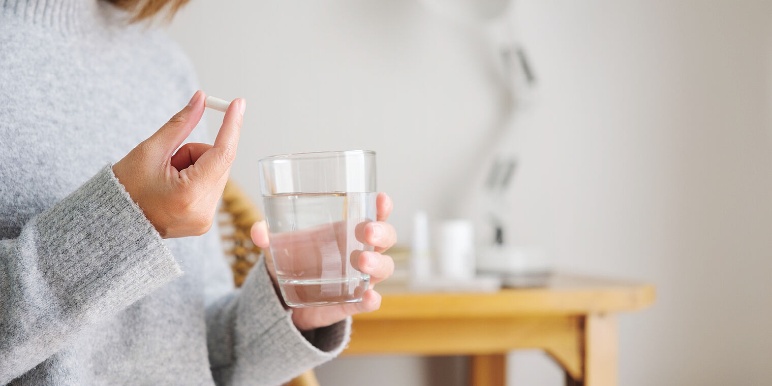 A person holding a glass of water and a pill, preparing to take the medication